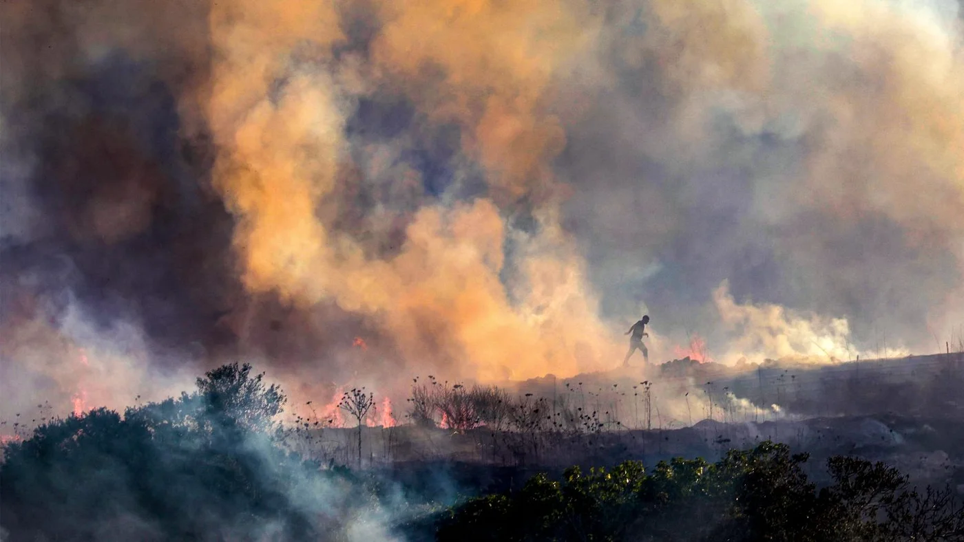 Palestinians walk through smoke from a fire near the village of Tell, west of Nablus in the occupied West Bank, after a reported settler attack, 18 July 2026 (Jaafar Ashtiyeh AFP).jpg
